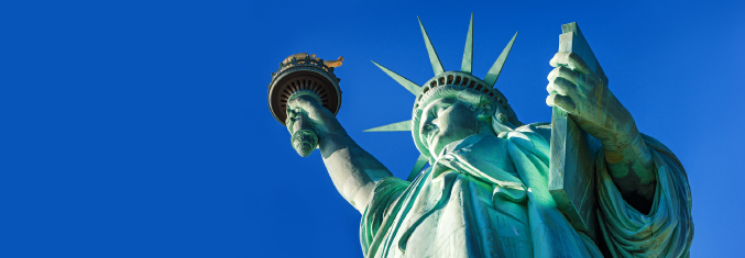 A view looking up from below the Statue of Liberty against a bright blue sky