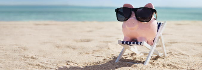 Pink piggy bank wearing sunglasses and sitting in a striped beach chair on the beach with the ocean in the background.